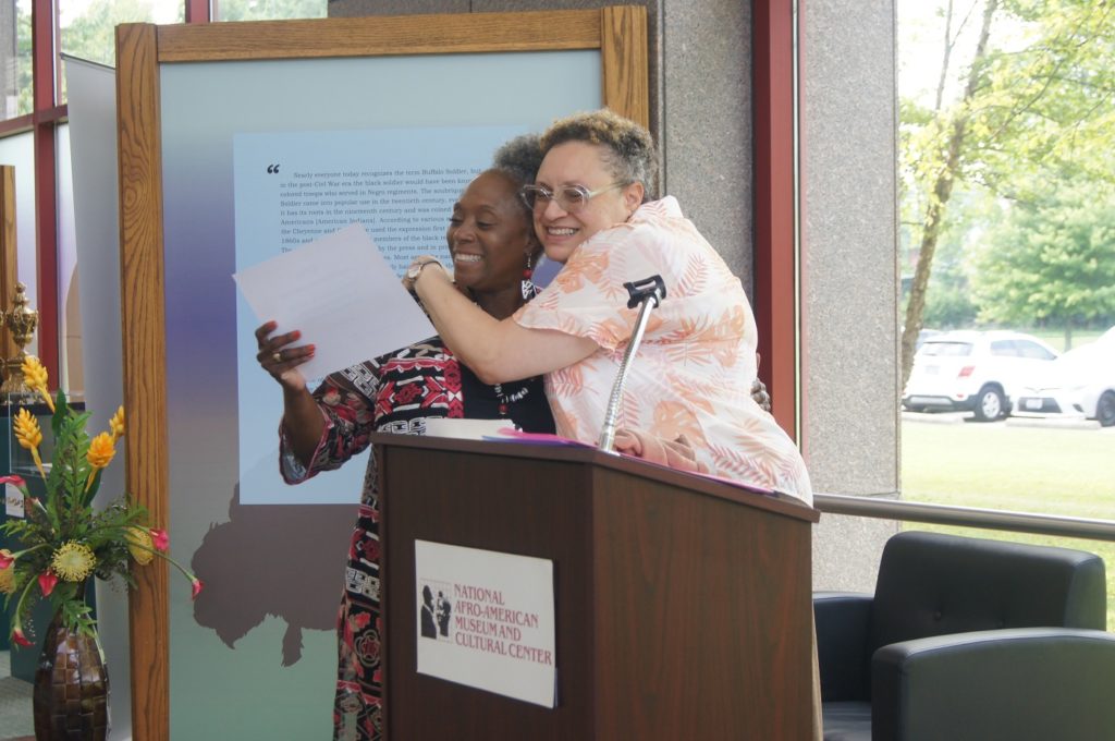 An image of an African-American women and white woman standing at a podium and hugging.