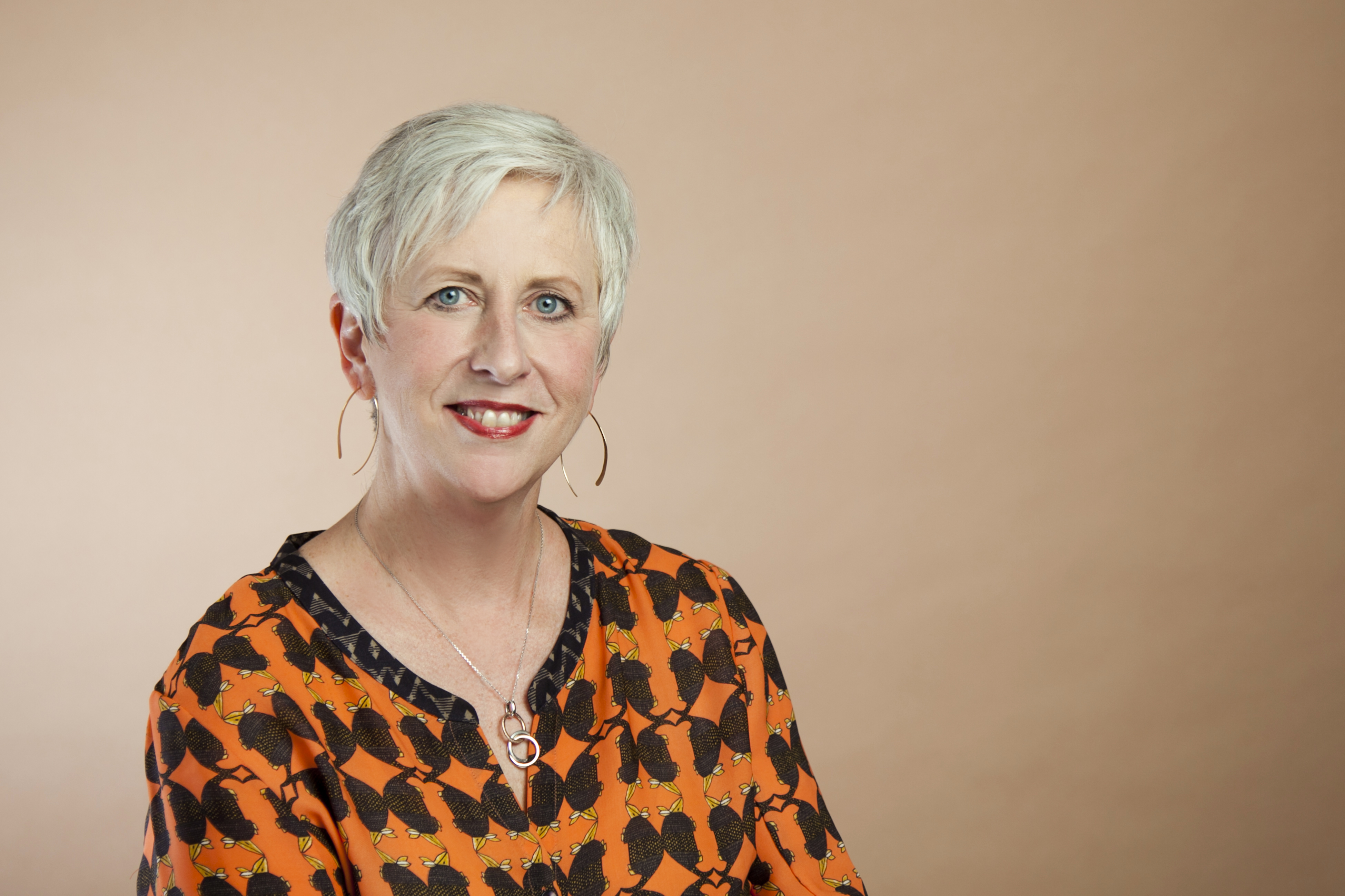 This is a photo of Teresa Bonner of Aroha Philanthropies. Teresa is seated and wearing a print top. She has short platinum hair.